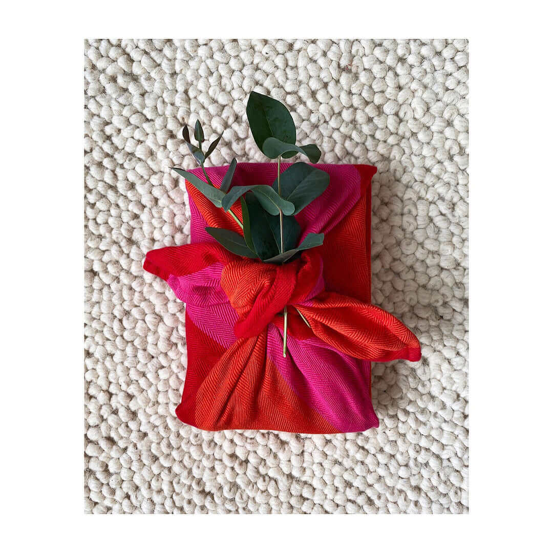 Red orange pink kitchen towel folded into a gift with a small green branch on top and a beige background carpet 