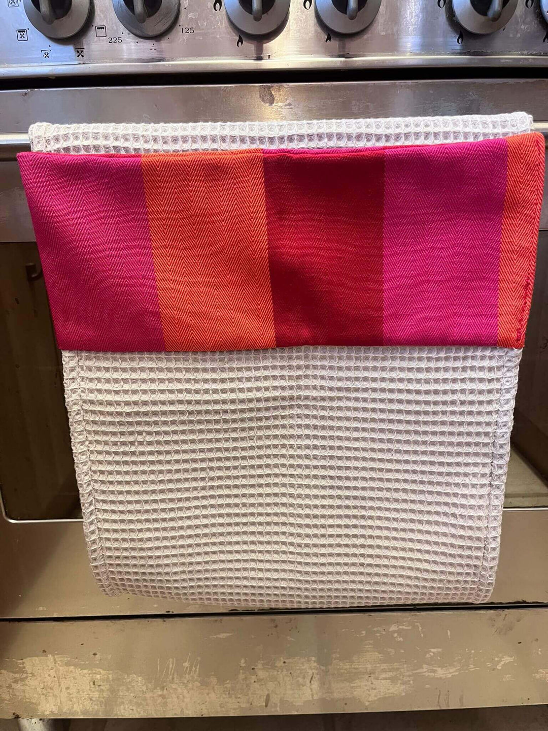 Roller towel beige cotton waffle with a red orange pink header close up shot hanging off a cooker bar