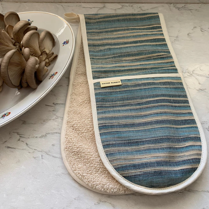 double oven glove with blue and sandy stripes on a marble white worktop next to a dish with fresh mushrooms
