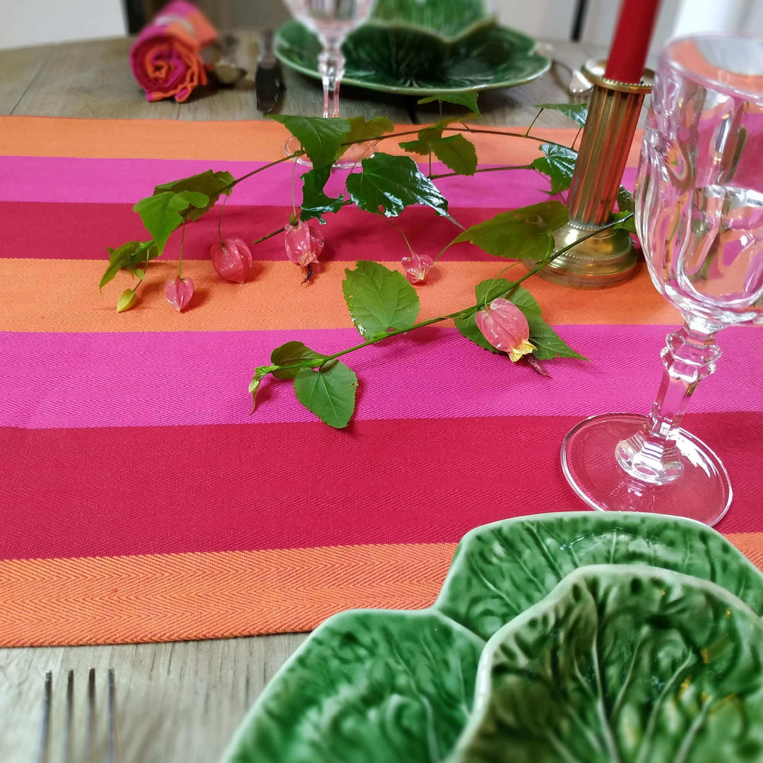 Close up on a red orange pink table runner with green plates in the shape of lettuce on the bottom and some wild flower on the top