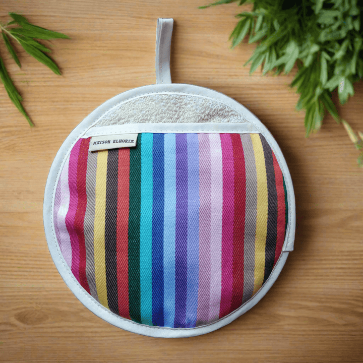 Rainbow round pot holder or pot grabber type oven mitt on a light table background with cooking herbs