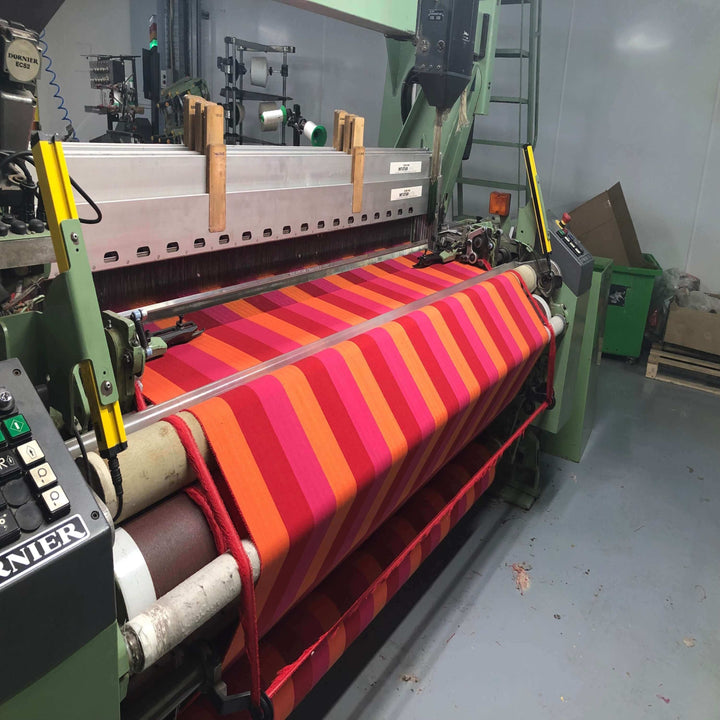 red orange and pink striped fabric on the loom, being woven