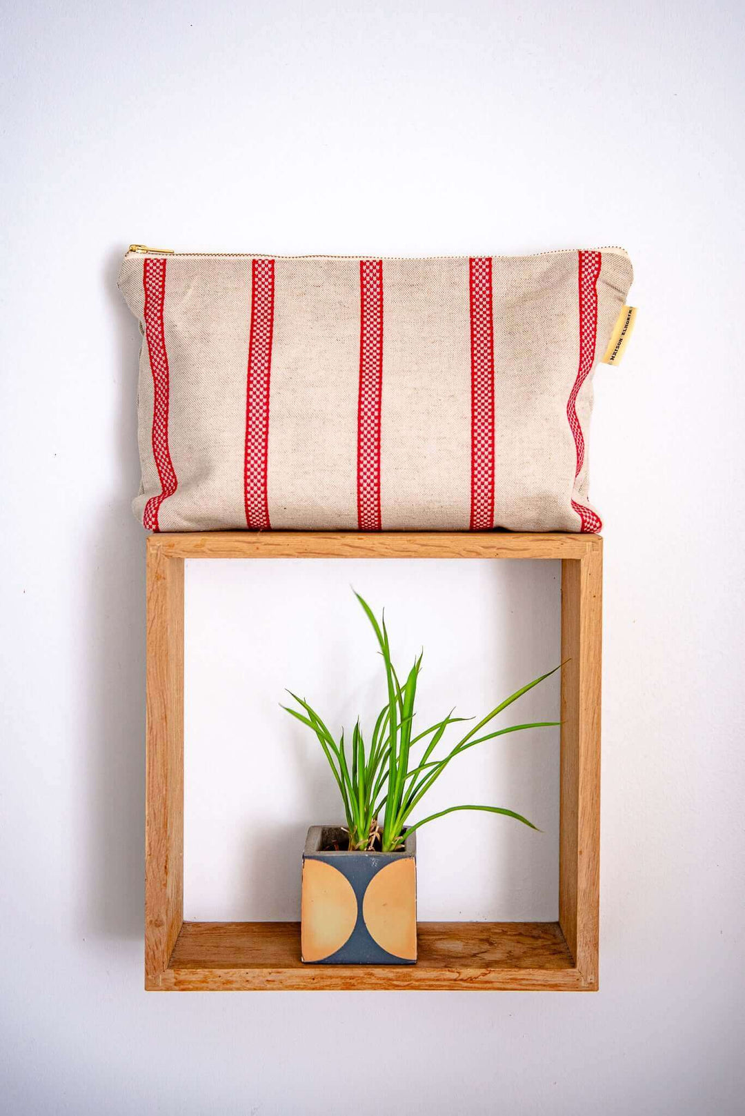 Red Striped linen toiletry bag on a wal wood frame with a small green plant below