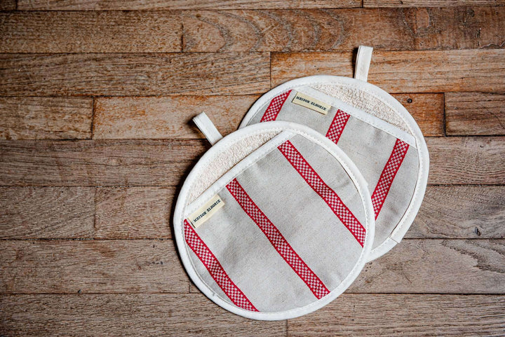 A pair of oven glove pot holder type off white with red embroided stripes on old wooden floor