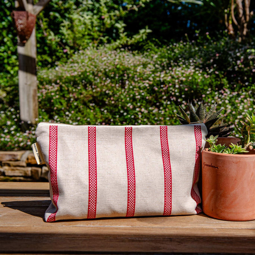 Toiletry bag or make up bag linen with old fashion French Style red stripes on a garden setting with a pot of green plants on the right and on a wooden table