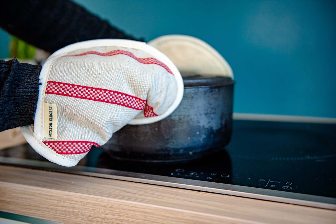 close up of a couple of linen and red striped embroided pot holders type oven gloves holding a pot. Portrait image focus on one of the gloves