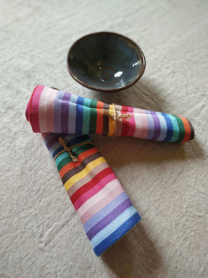 2 Rainbow napkins cotton rolled up besides a blue bowl