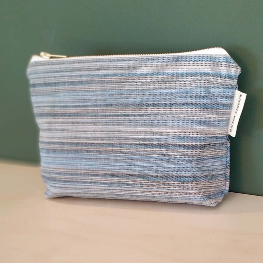 Blue striped boy toiletry bag on a off white support and green back drop