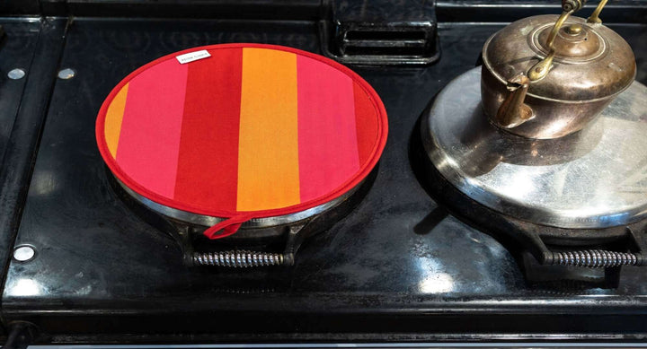 Aga chef pad red orange pink on an Aga with and antique kettle on the other hob on the right , view close up from  above