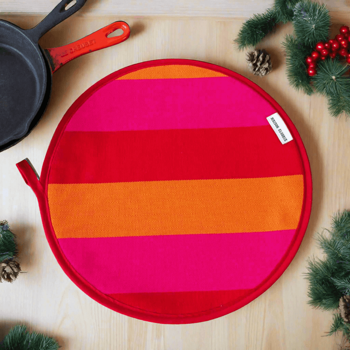 Red Orange pink striped premium quality insulating Aga hob plate cover on wooden surface with cast iron pans and Christmas branches and pine cones