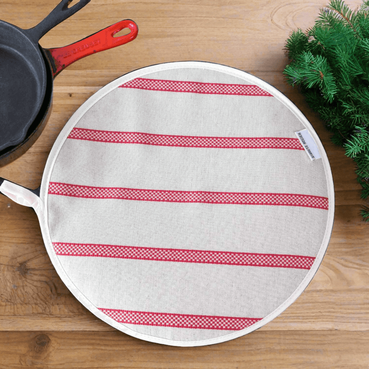 Linen union with red stripes insulating Aga hob plate cover on wooden surface with cast iron pans and Christmas green branch
