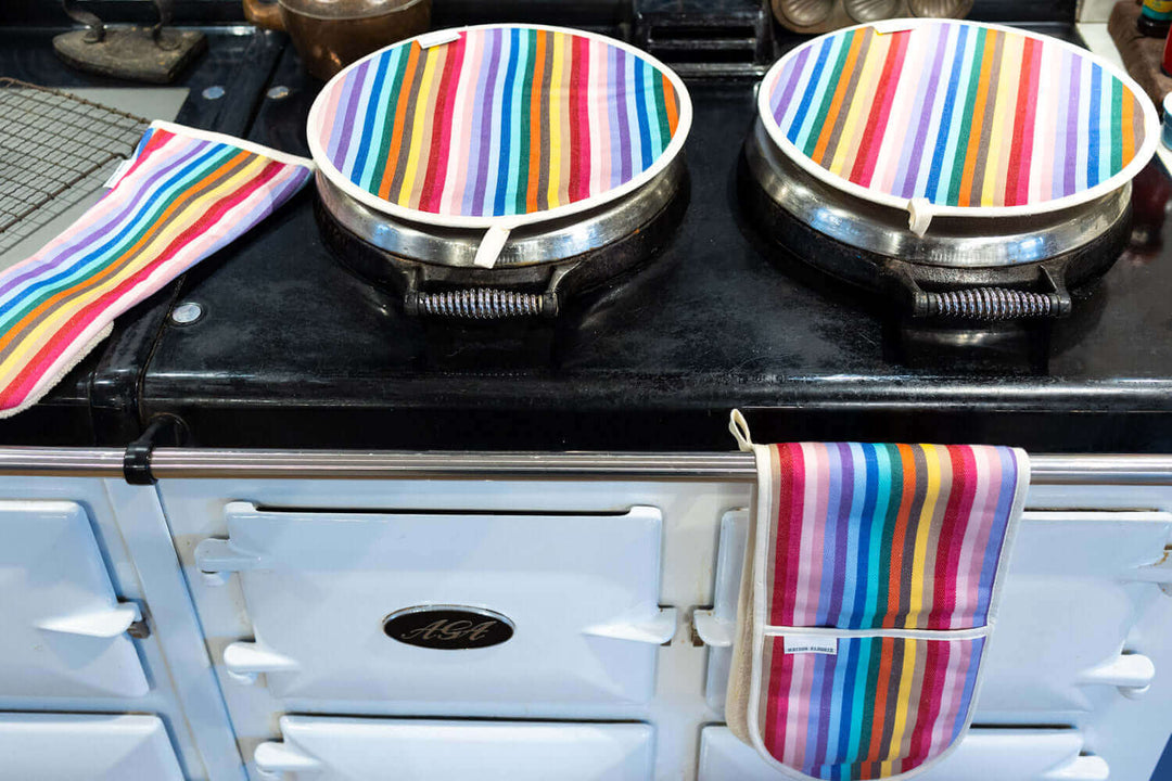 Pale blue Aga range cooker showing from above a pair of matching rainbow hob covers, a long oven glove, a double oven gloves