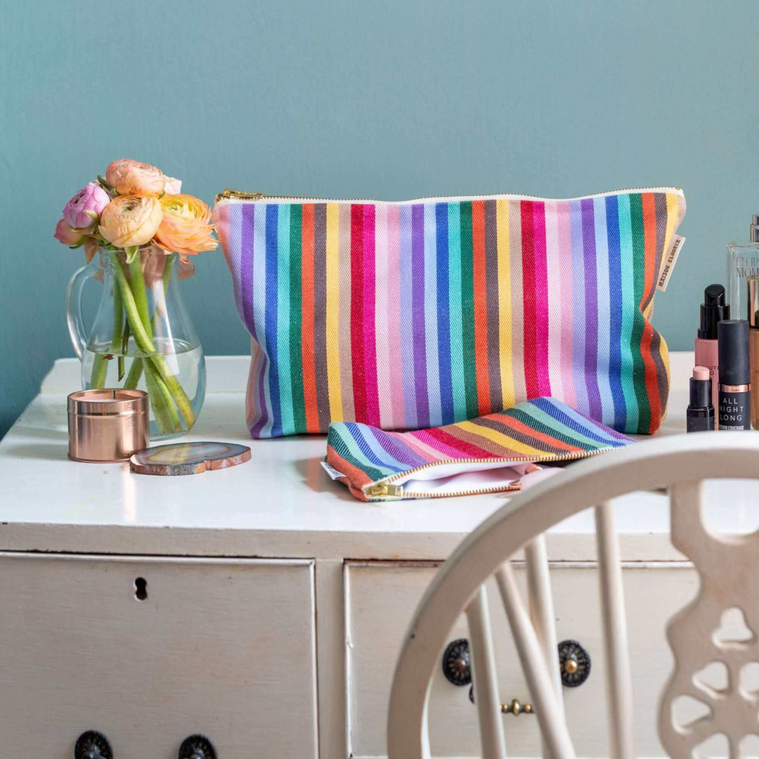 White make up table with a rainbow wash bag and a fresh flower near it 