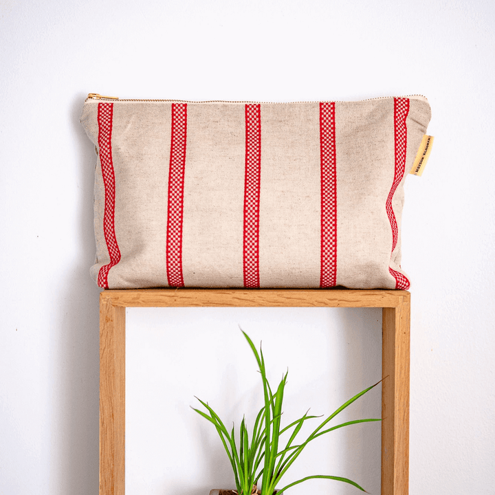 Large red Striped linen toiletry bag on a wal wood frame with a small green plant below