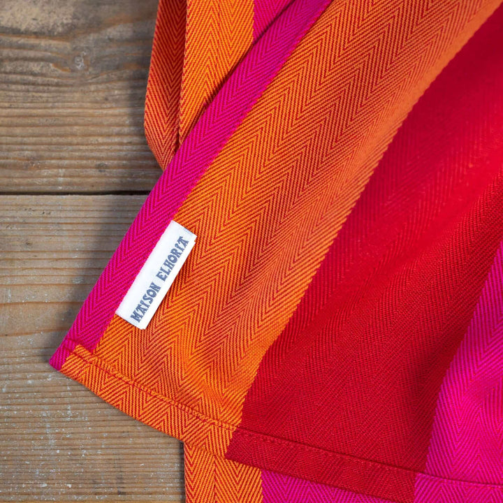 Tea towel red orange pink wide striped showing a white label 'Maison Elhoria' on a wooden surface