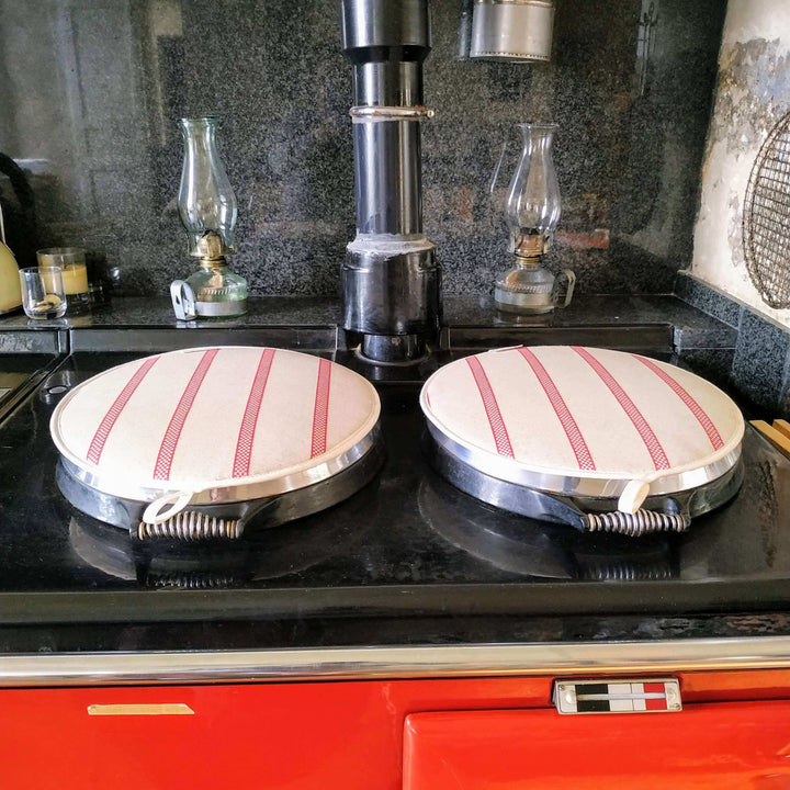 Two Linen union with Red stripes insulating Aga hob plate cover on Aga with 2 petrol lamps in the background