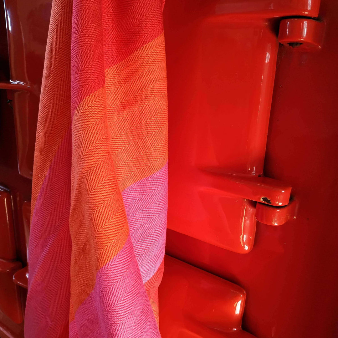 Red orange pink striped kitchen towel hanging against a red Aga 's oven doors