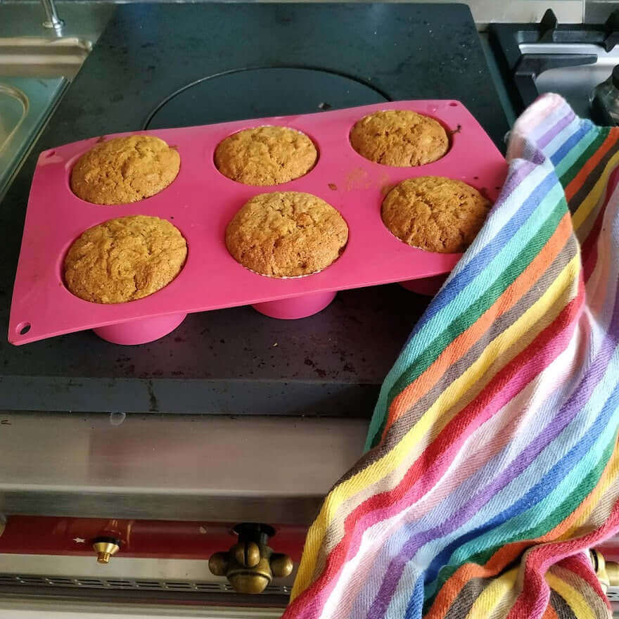 muffins just baked into a pink silicone mold with a rainbow kitchen towel on the right bottom corner