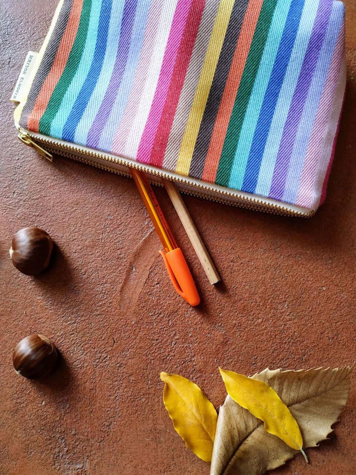 rainbow pencil case open with 2 pen partly out , a couple of chestnuts and a dried tree leaf on a terracotta floor