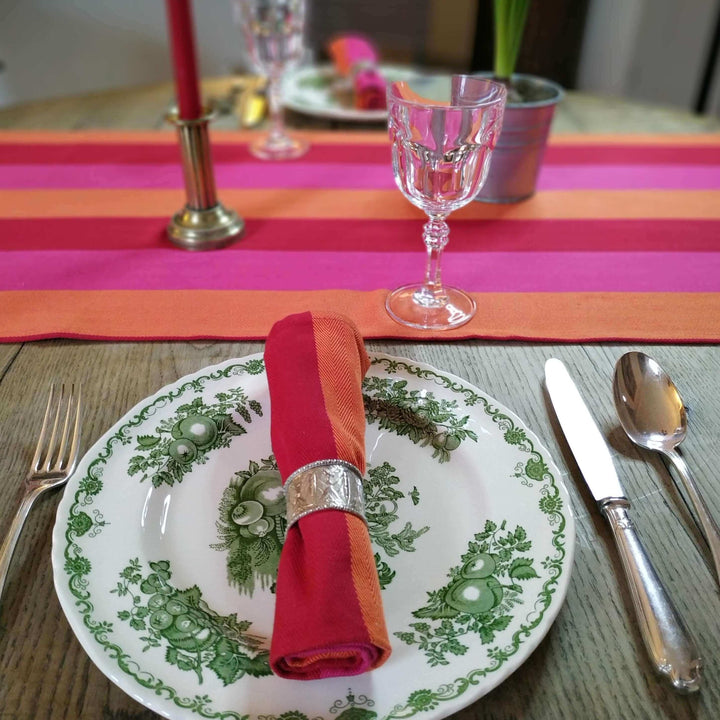 table runner and napkin red orange pink organic and recycled cotton fabric on a wooden table with a glass and a antique plate in the front and red candle in the middle