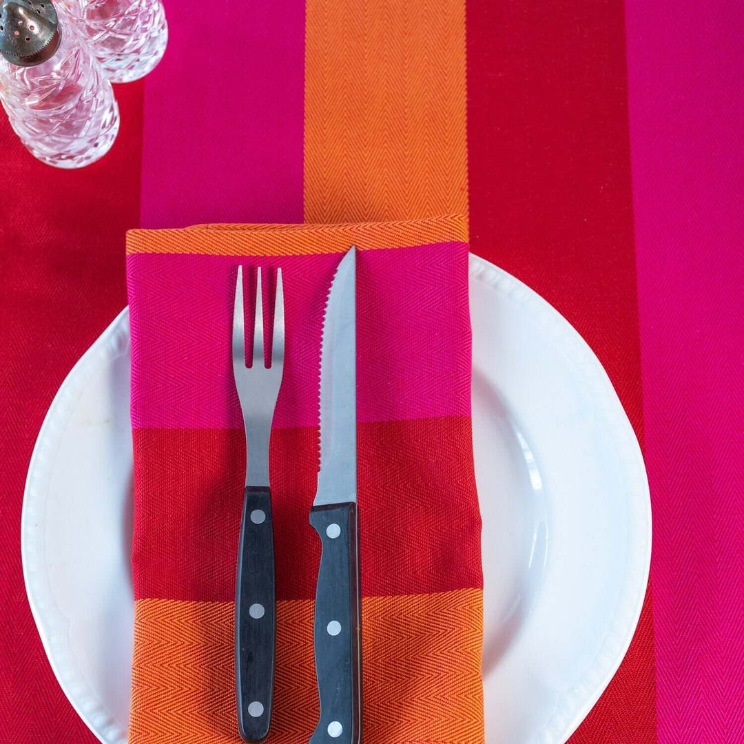 Tablecloth Red Orange pink organic cotton with plate with organic red orange pink cotton napkin on it , with knife and fork on top and salt and pepper pots   on the corner