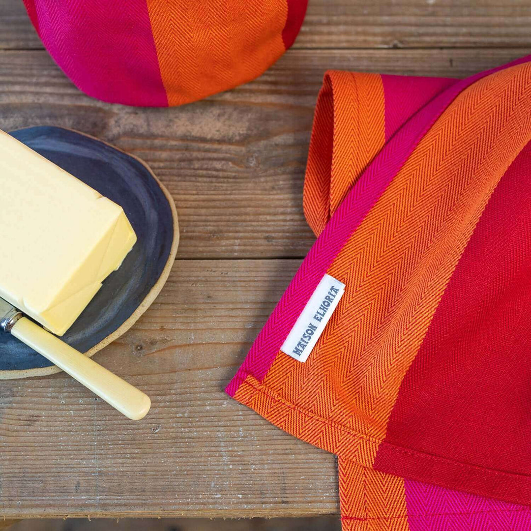 red orange pink organic cotton napkin with butter on a plate and knife on a wodden table
