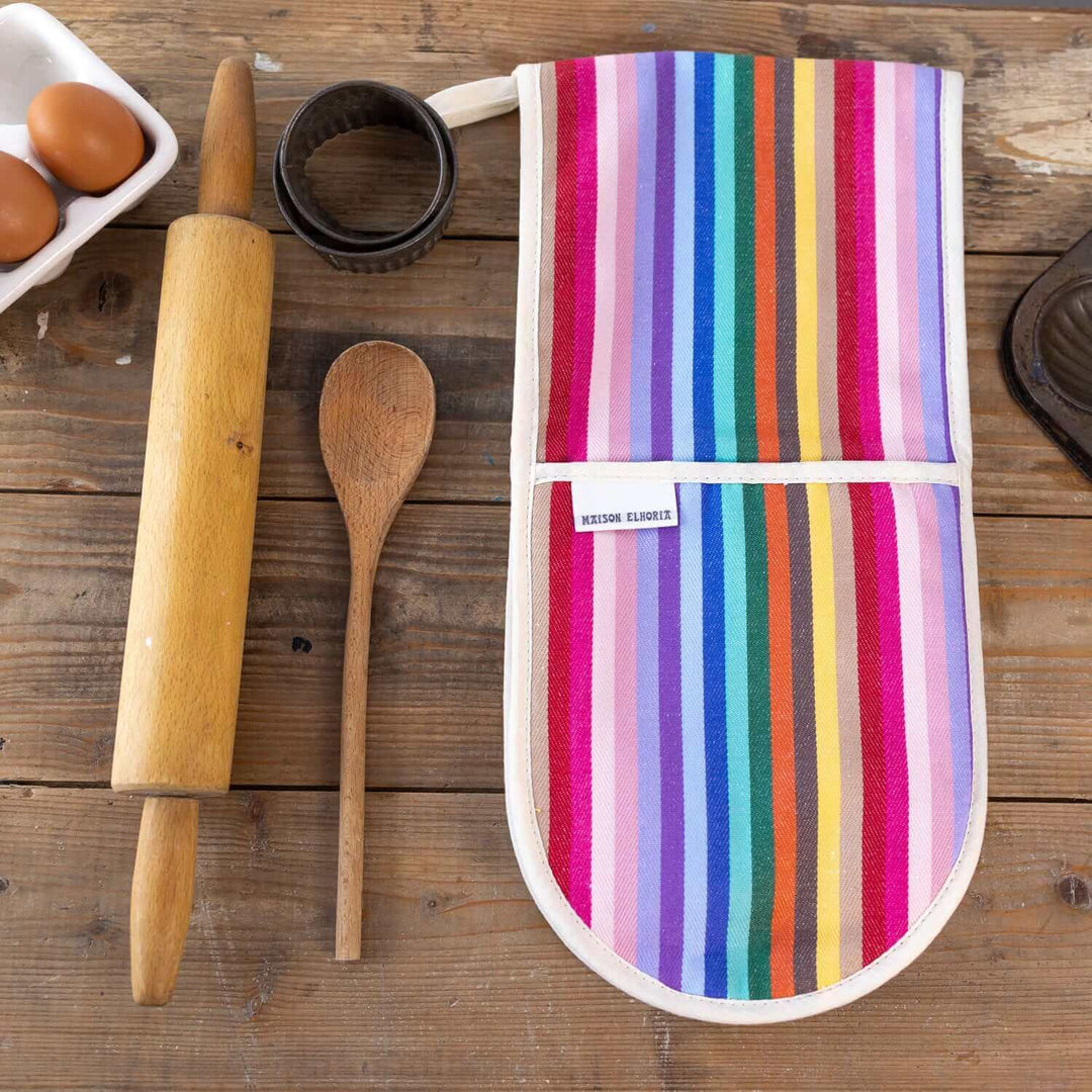 Premium organic cotton double oven gloves with rainbow stripes on wooden table with baking accessories and eggs