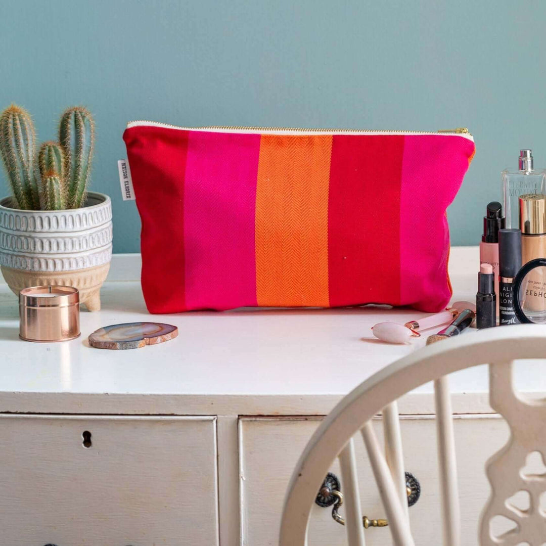 red orange pink wash bag on a white dressing table with a cactus plant and the back of a chair